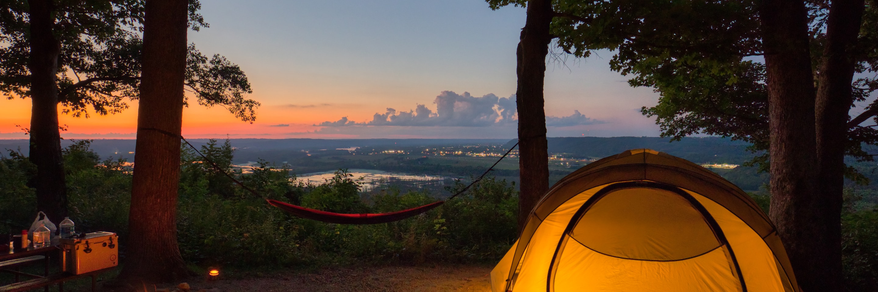 Glowing tent and hammock at a valley overlook at sunset